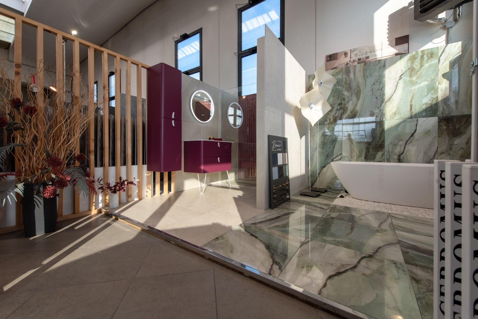 Esposizione di un bagno in showroom con mobiletto viola, piastrelle in marmo e vasca da bagno indipendente.