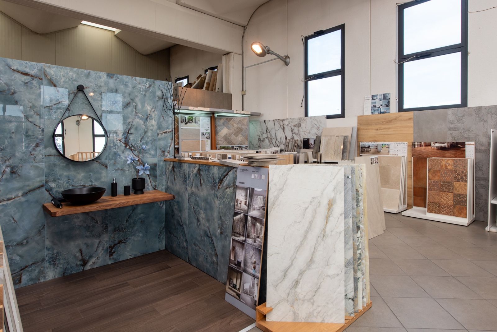 Showroom di piastrelle che espone vari modelli e colori, con un'esposizione per il bagno dotata di specchio e lavandino.