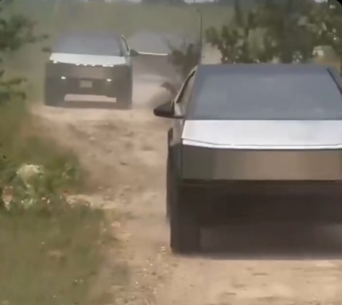Two tesla cars are driving down a dirt road.
