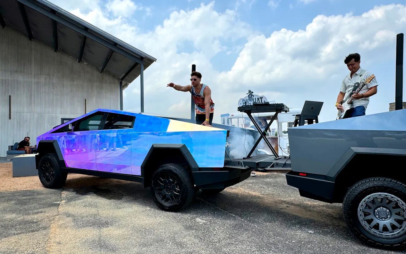 A tesla cybertruck with a trailer attached to it is parked in front of a building.