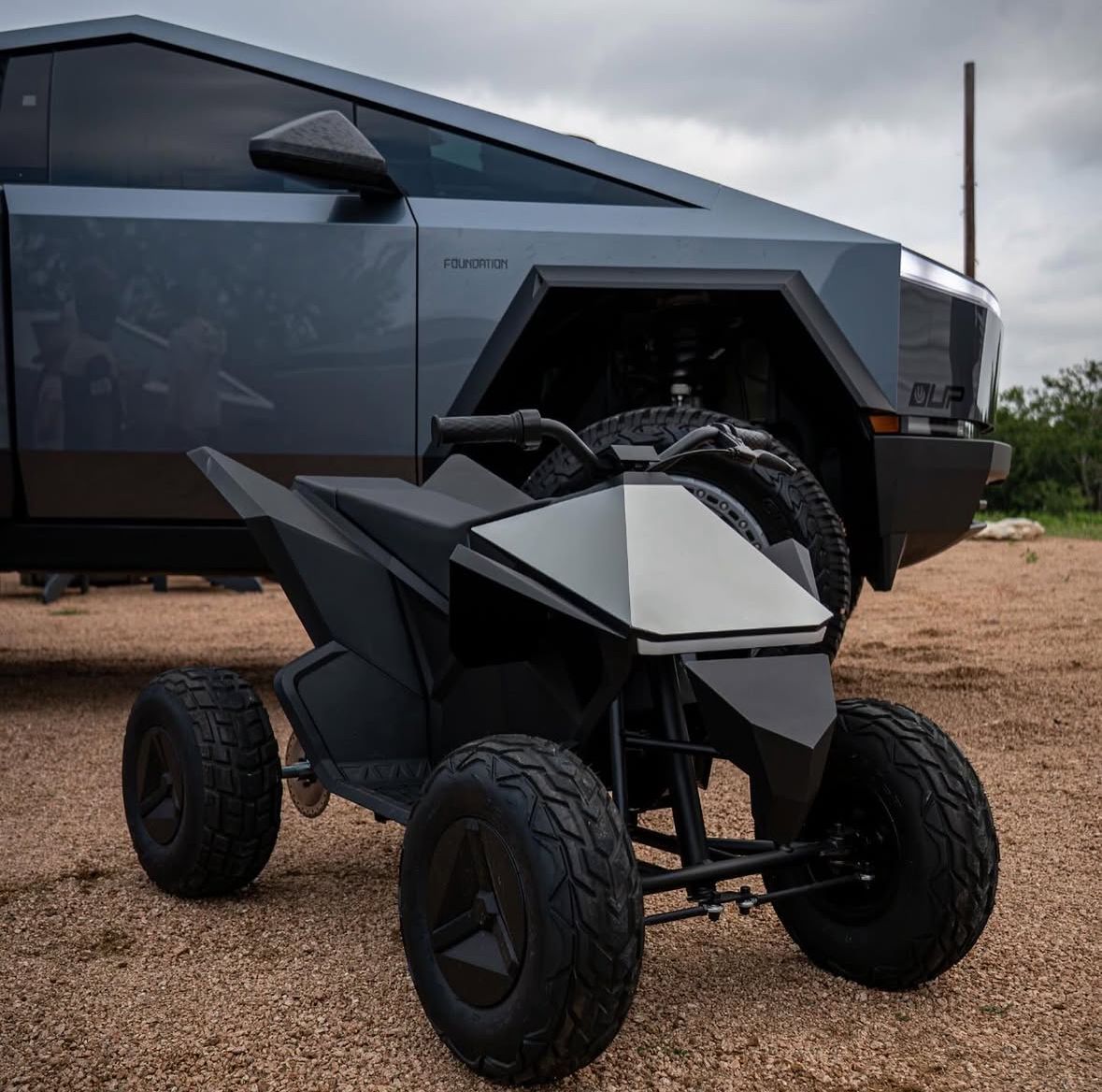 A tesla cybertruck is parked next to a small atv