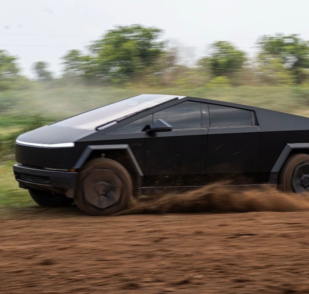 A black tesla cybertruck is driving through a dirt field