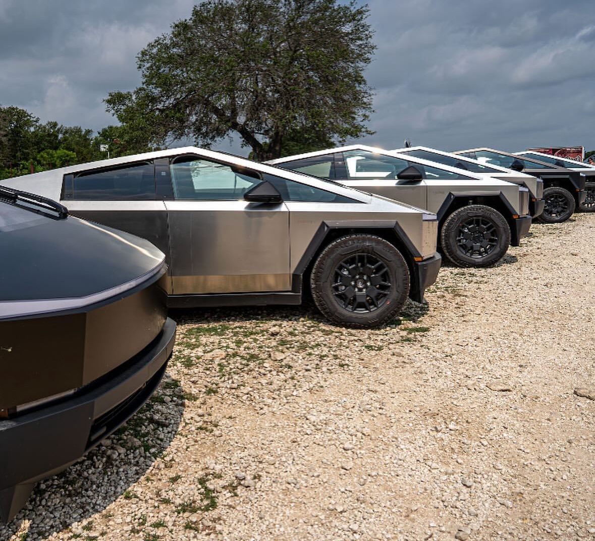 A row of tesla cars are parked in a gravel lot.