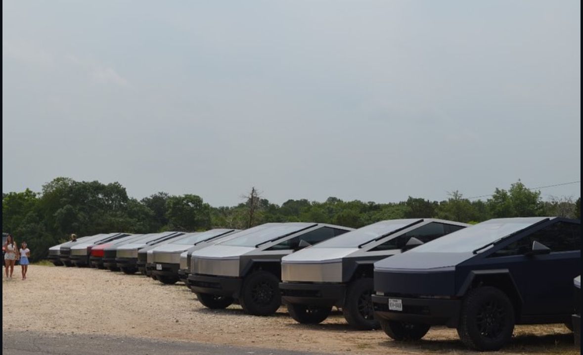A row of tesla cars are parked in a gravel lot