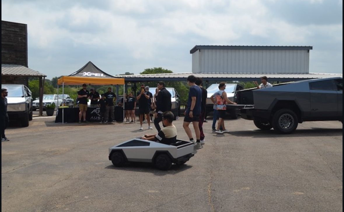 A boy is driving a small toy car in a parking lot.
