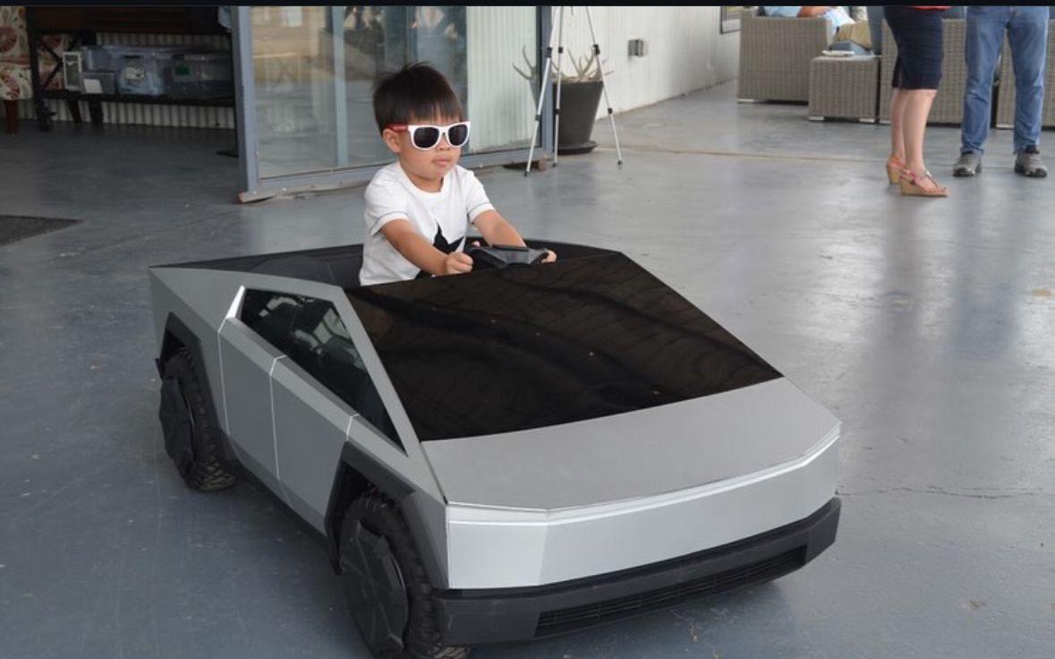 A young boy wearing sunglasses is driving a toy car.