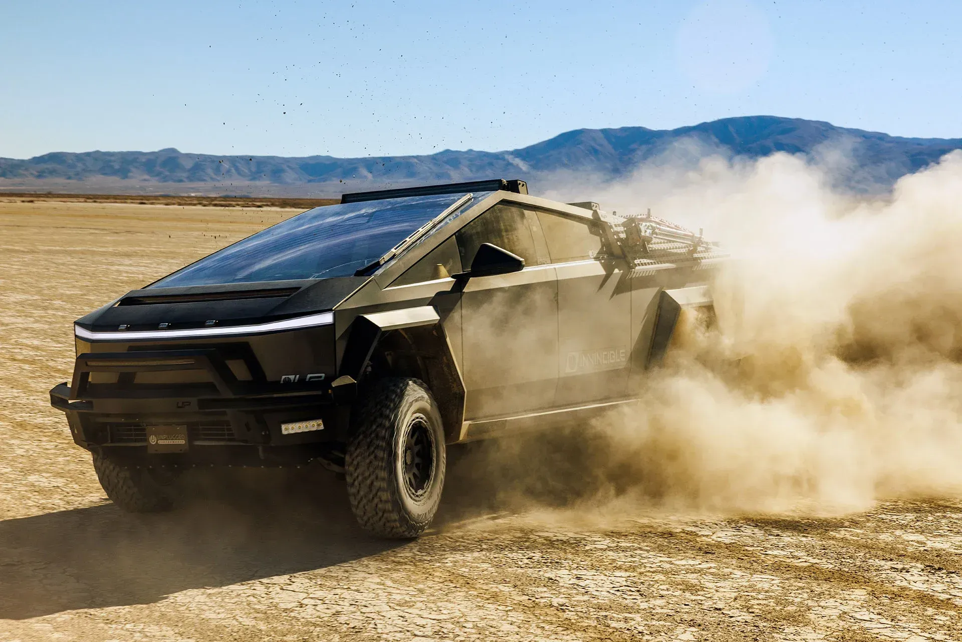 A tesla cybertruck is driving through a dirt field.
