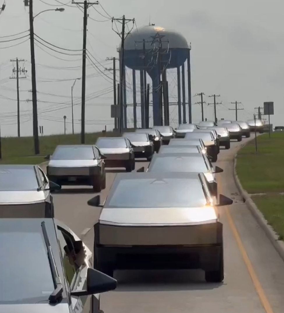 A row of cars are driving down a road with a water tower in the background