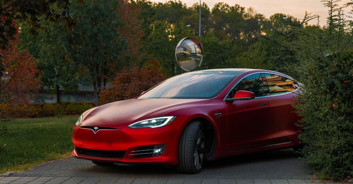 A red tesla model s is parked in a driveway next to a bush.