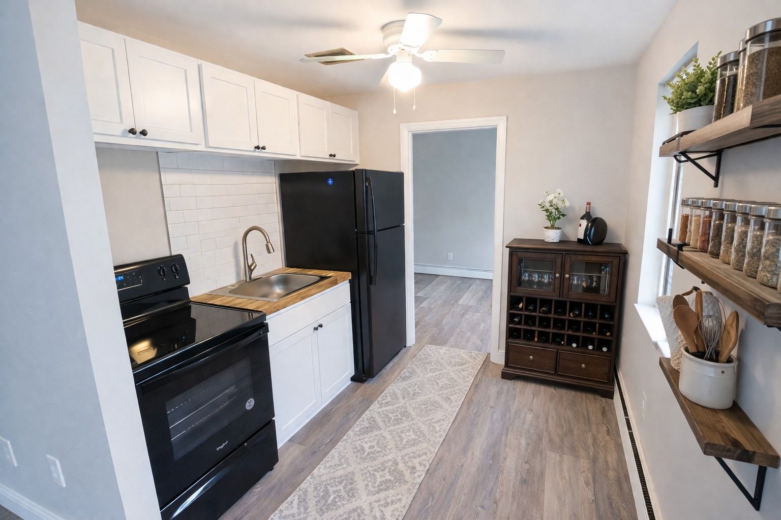 A small kitchen with white cabinets, a black stove and refrigerator, a wood countertop, and wall-mounted wooden shelves.