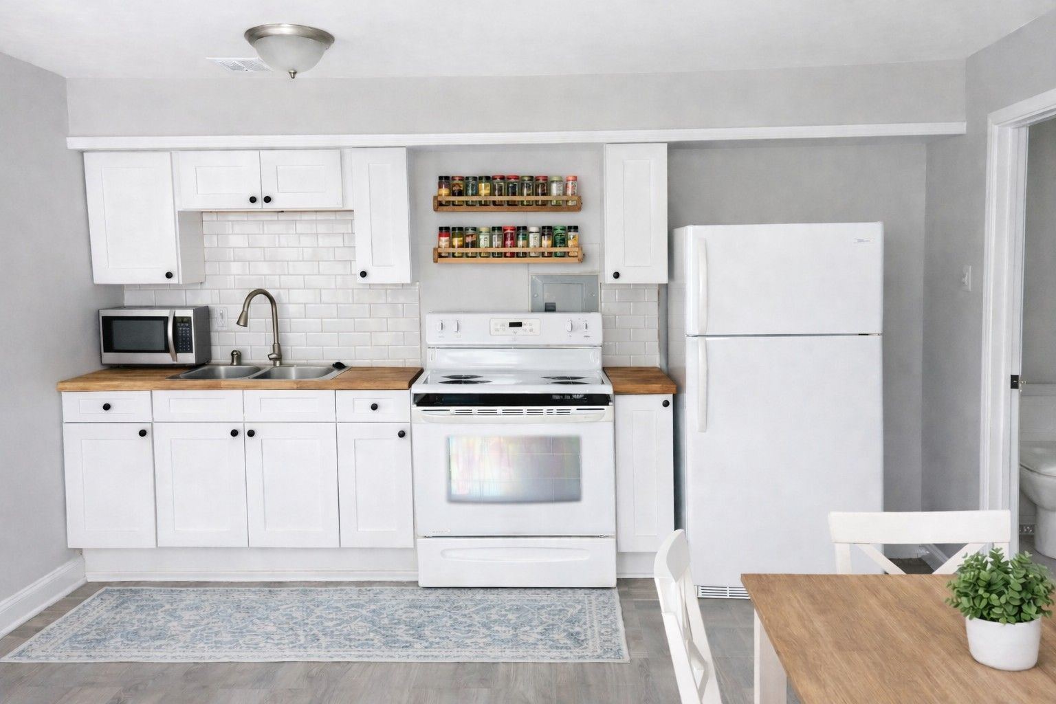 A bright kitchen with white cabinets, light wood countertops, a white oven, a refrigerator, and a small spice rack.
