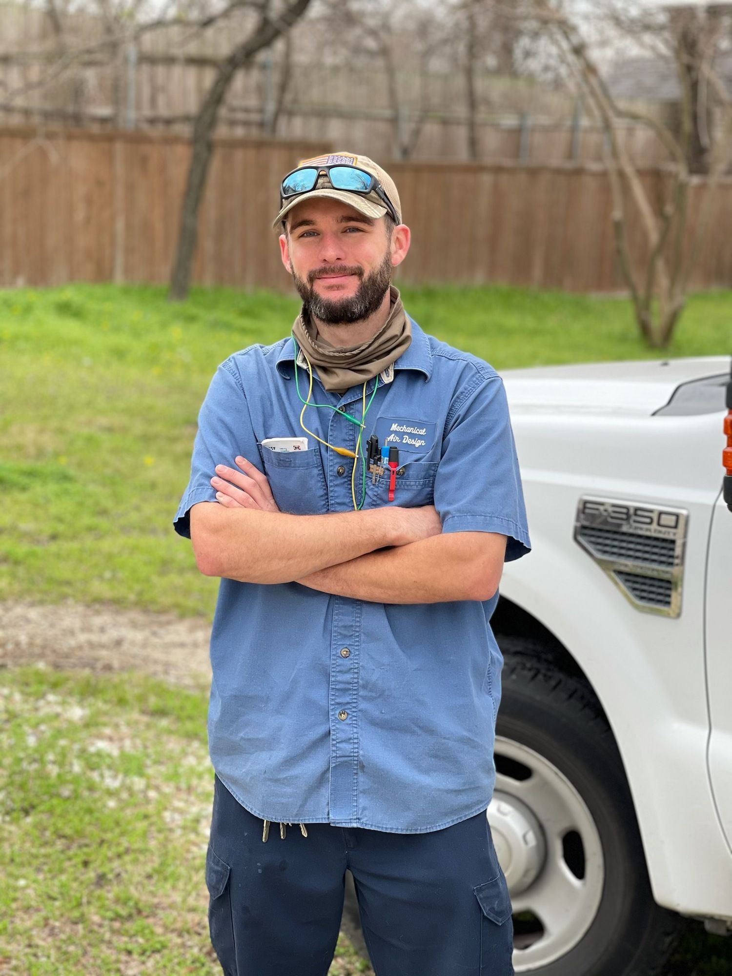 A man is standing in front of a white truck with his arms crossed.