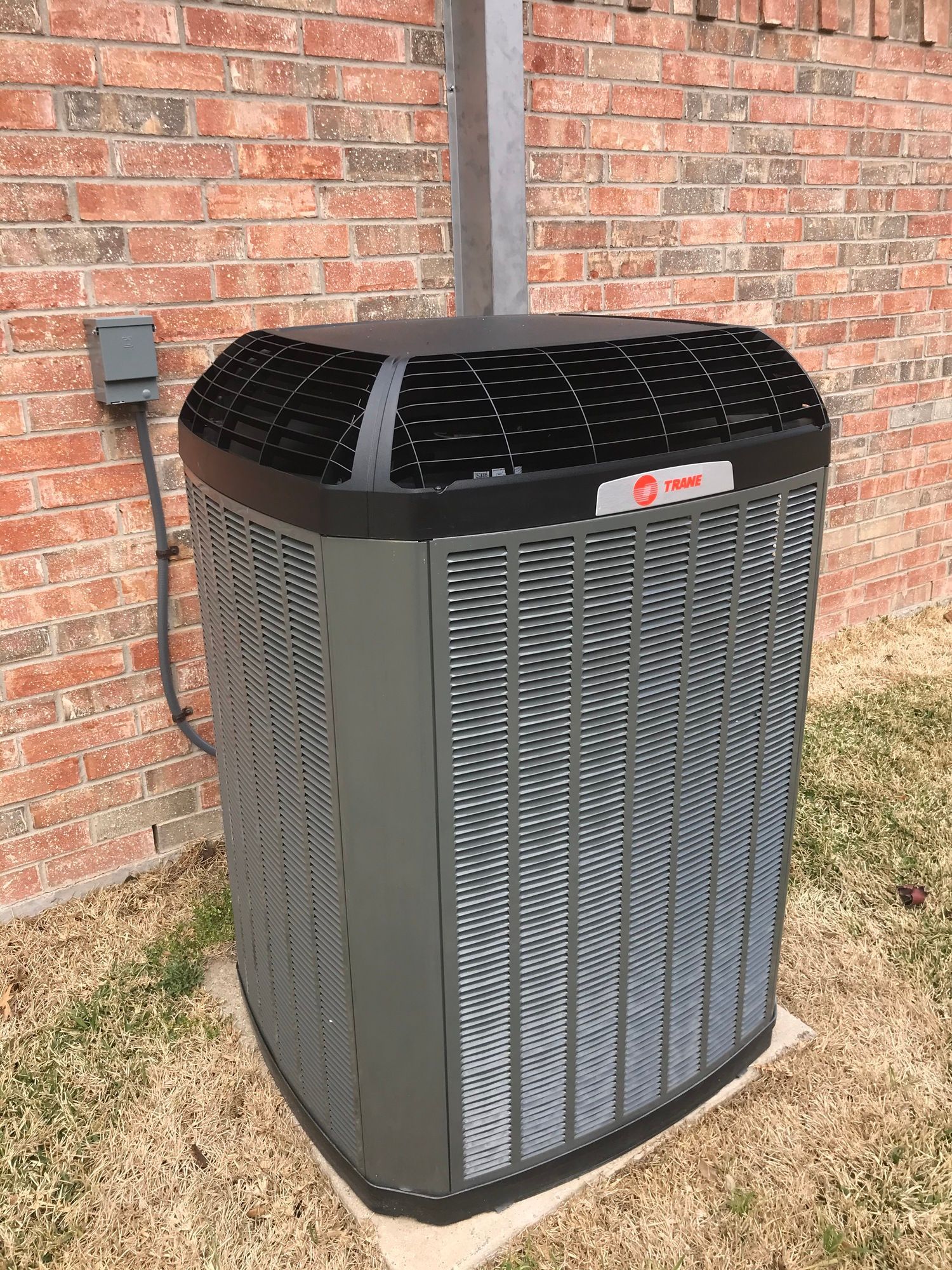 A large air conditioner is sitting in front of a brick wall.