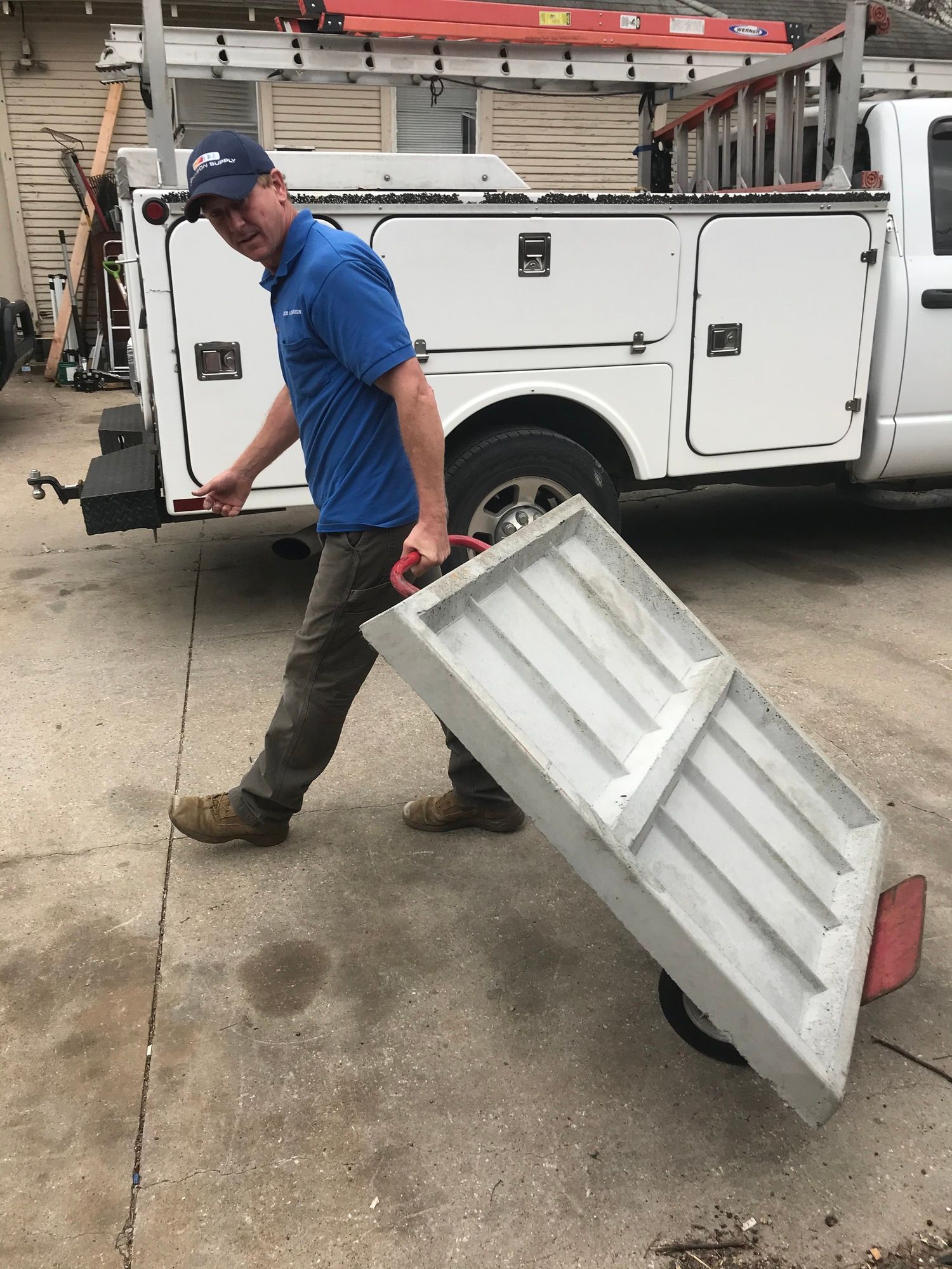 A man is pushing a door on a cart in front of a truck.
