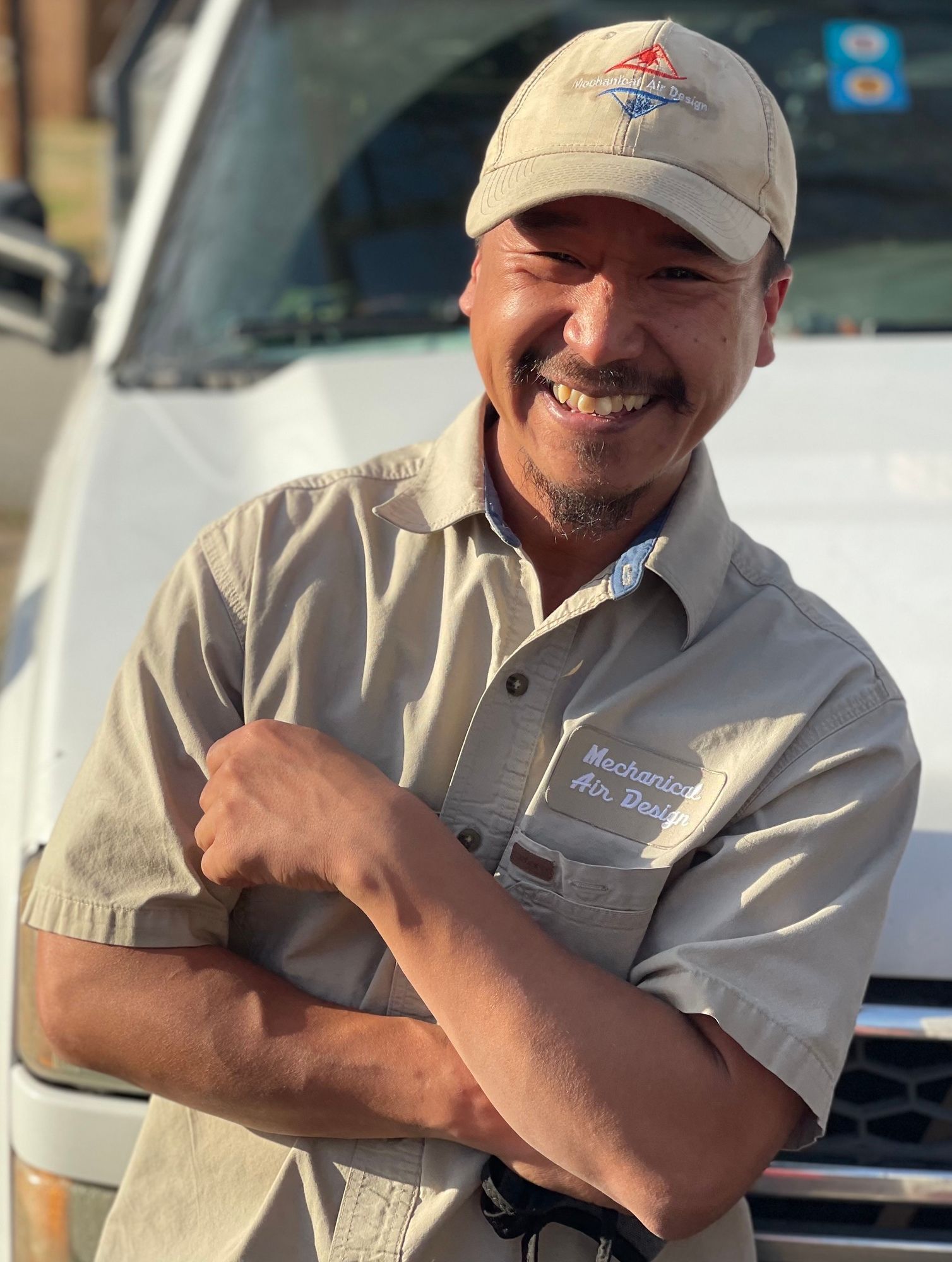 A man with his arms crossed is smiling in front of a white truck.