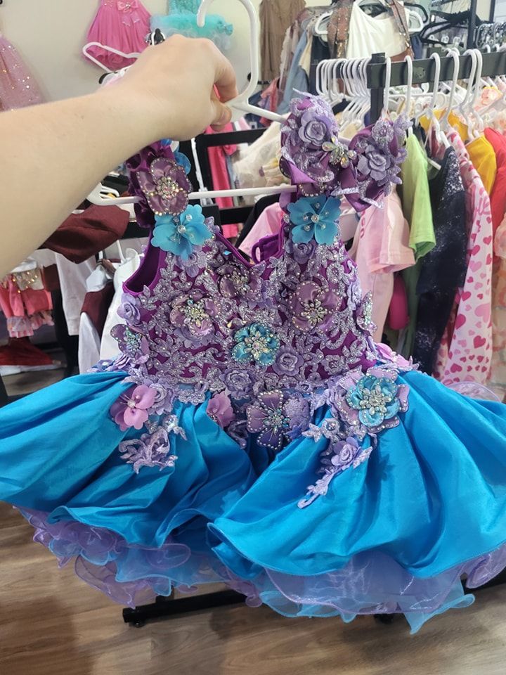 A person is holding a blue dress with purple flowers on it