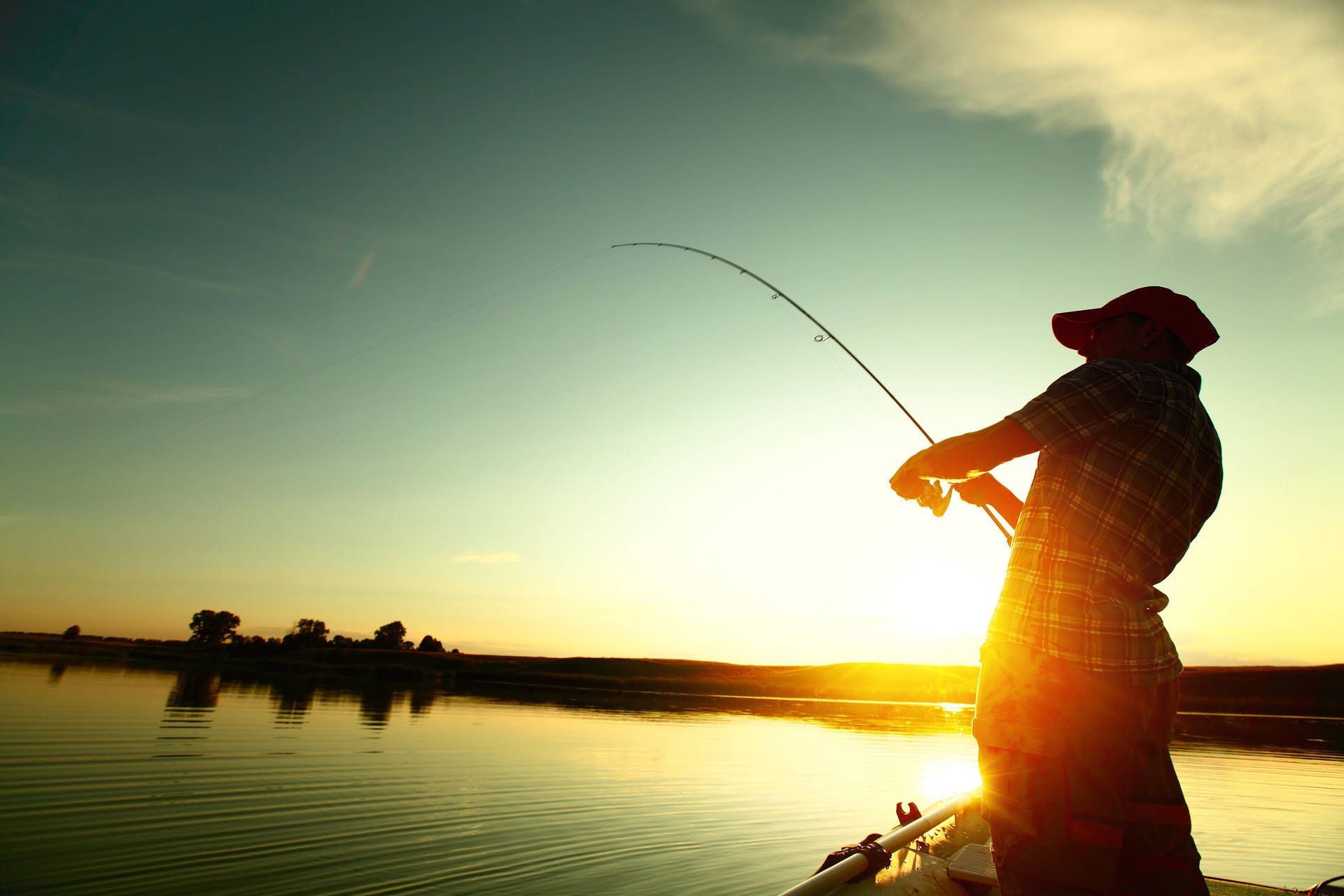 Person fishing at sunset, silhouette, rod bent, water, trees.