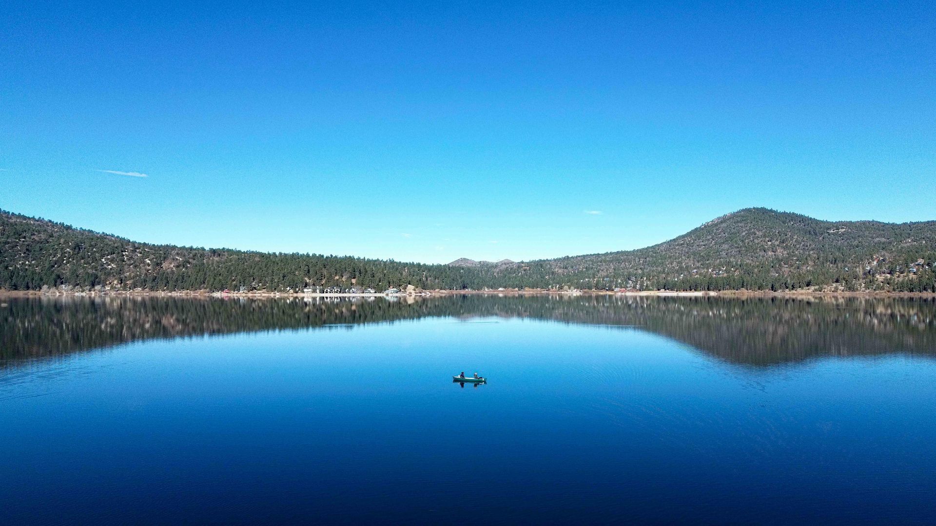 Calm lake reflects mountains and clear blue sky. A small boat is in the center.