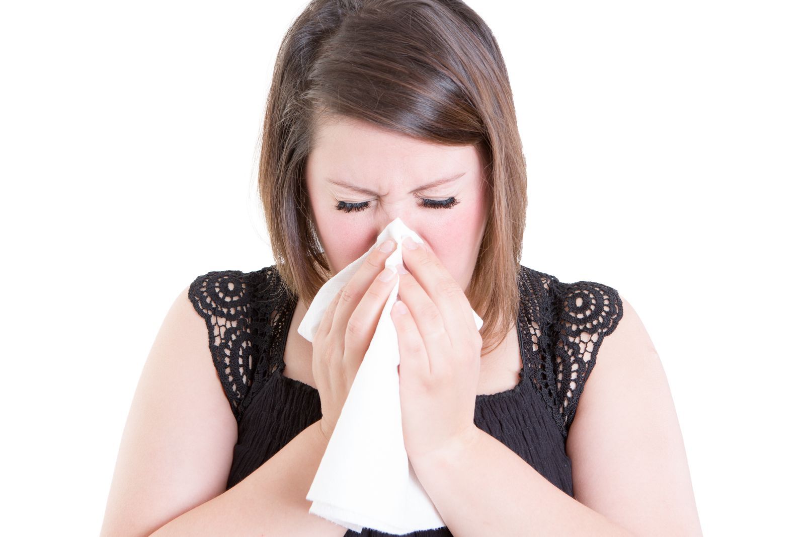 A woman forcefully blowing her nose into a tissue