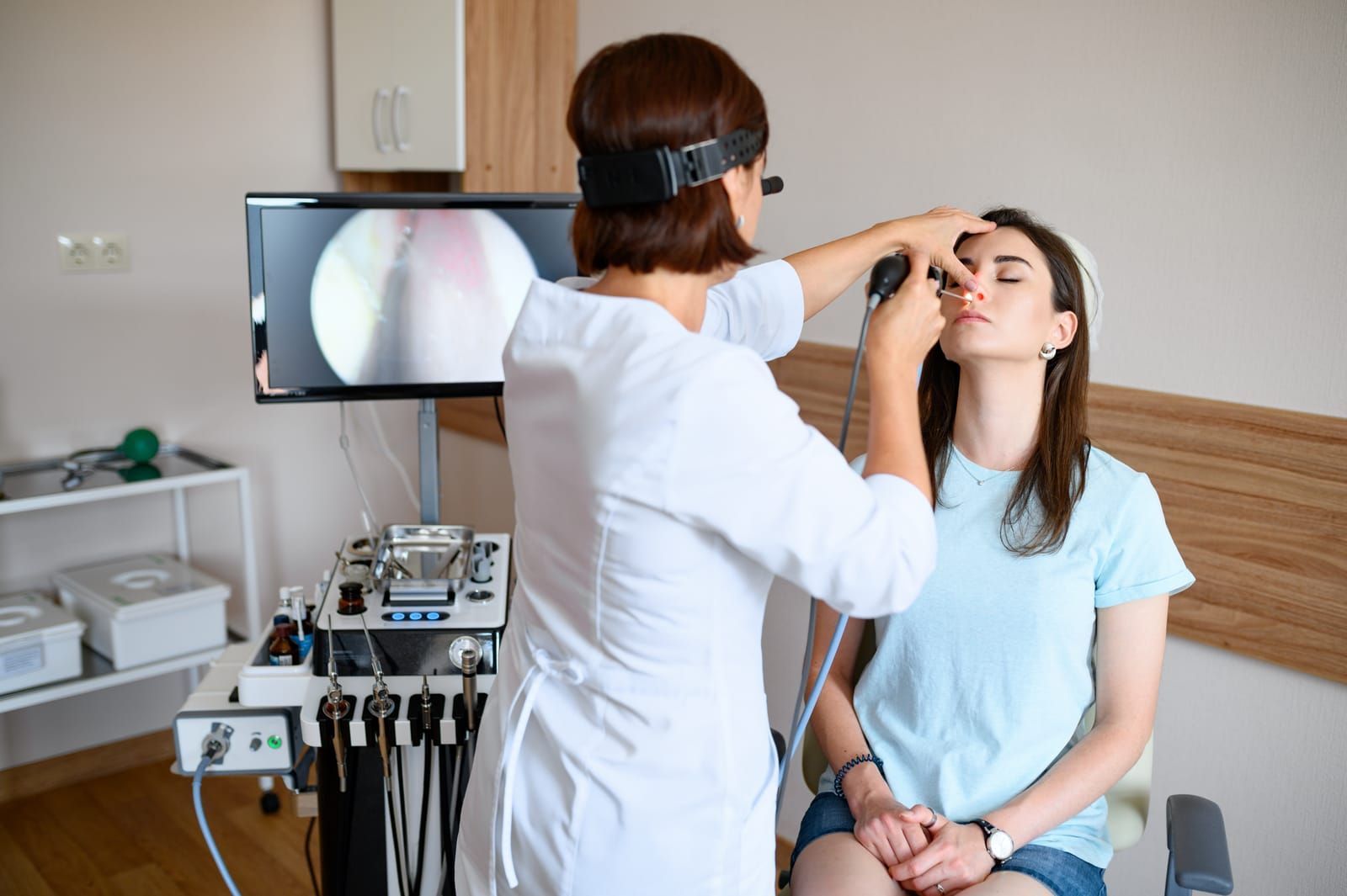 Doctor examining patient's nose with an endoscope, medical setting with monitor displaying nasal passage.