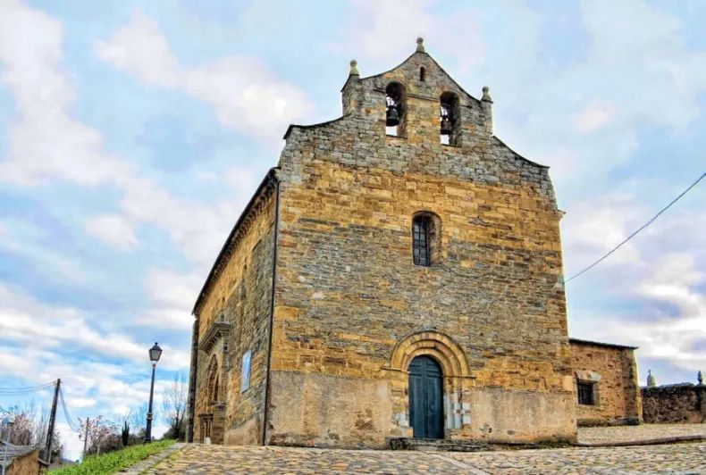 Medieval stone church with arched doorway and bell tower under a cloudy sky.