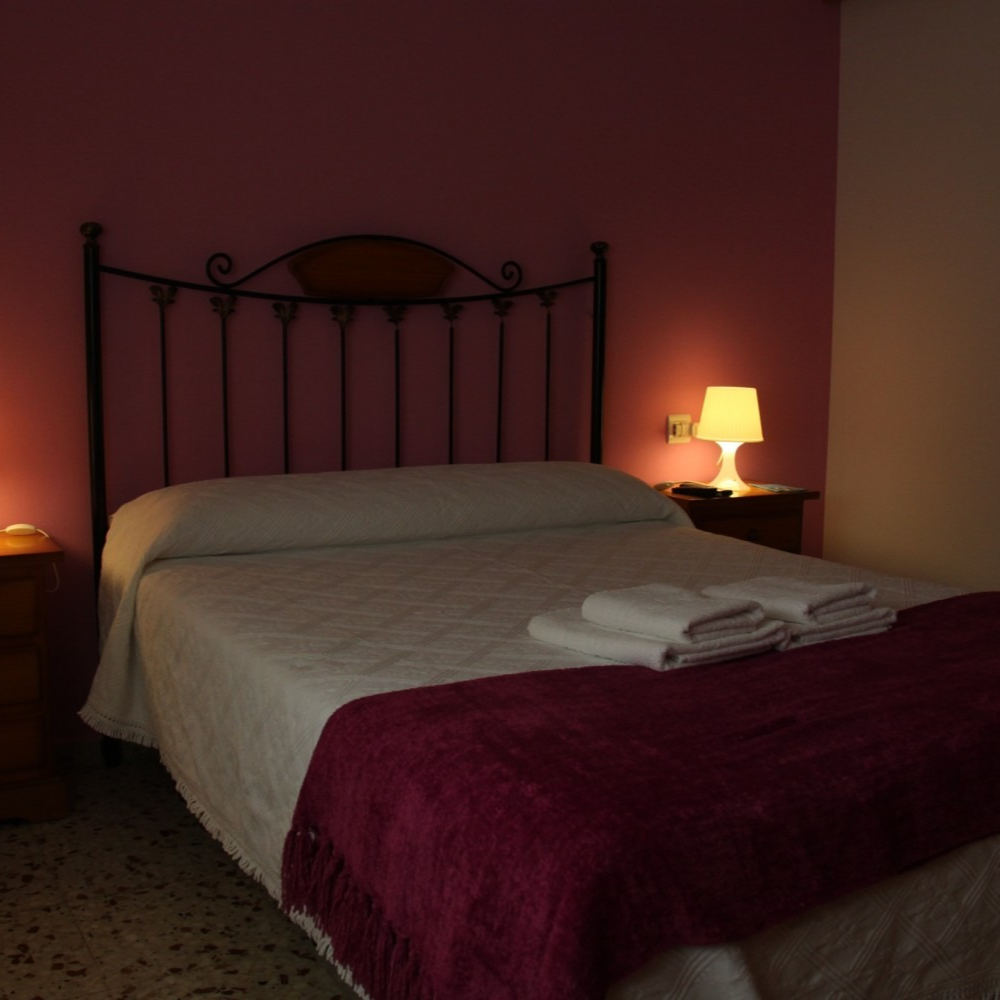 A bedroom with a bed and a lamp on the nightstand