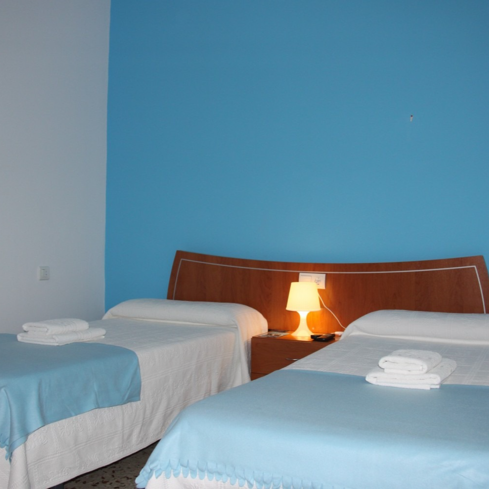 A bedroom with two beds and a lamp on the nightstand