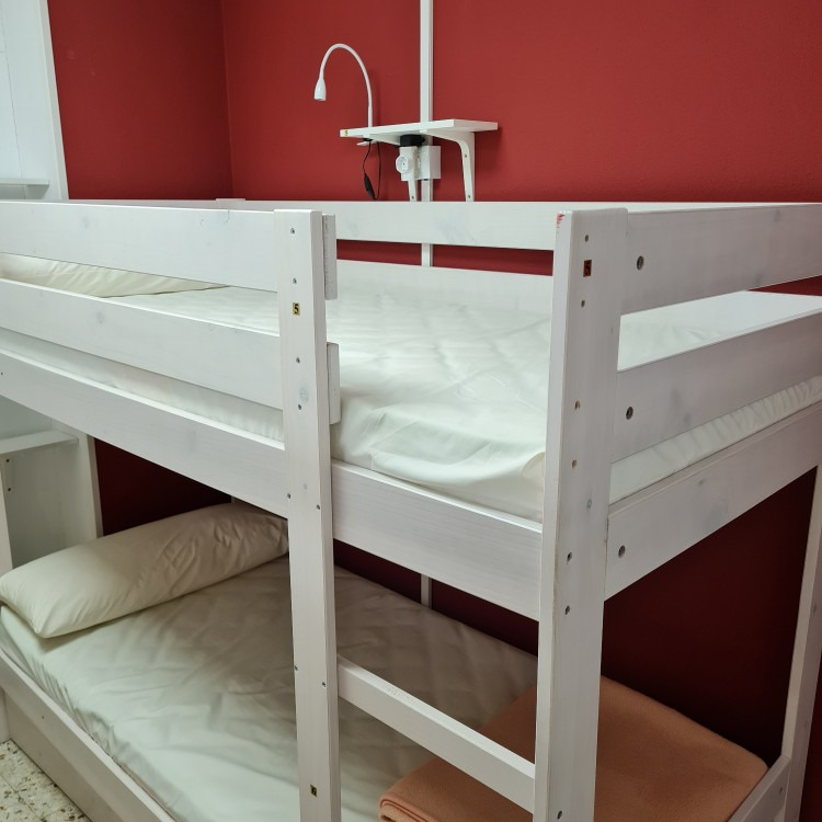 A white bunk bed with a red wall behind it