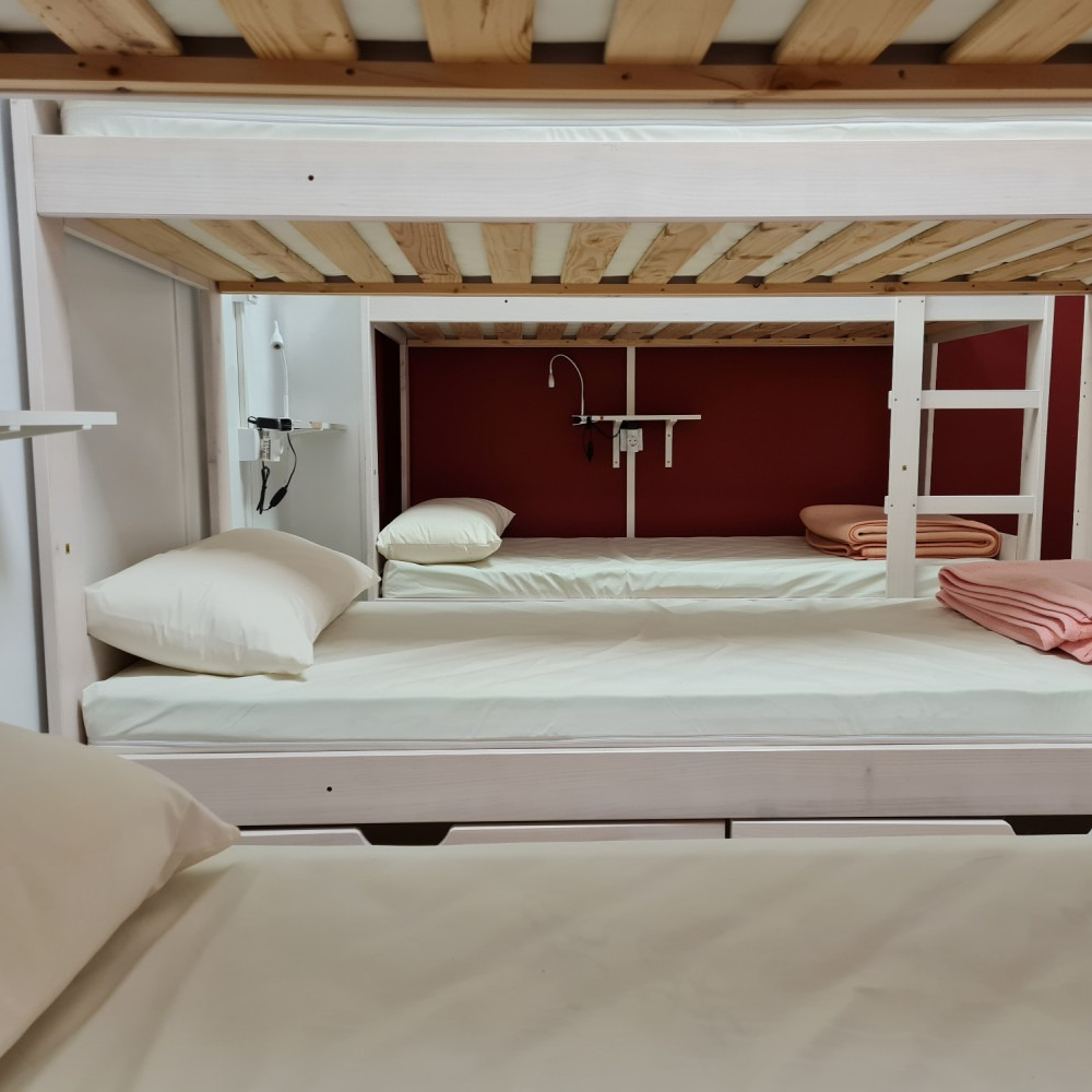 A bunk bed with white sheets and a red wall