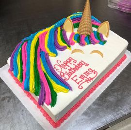 Unicorn-themed birthday cake with rainbow mane, gold horn, and “Happy Birthday Emma” icing on a white tray