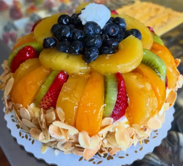 Fruit tart topped with blueberries, kiwi, peaches, strawberries, and whipped cream on a white plate
