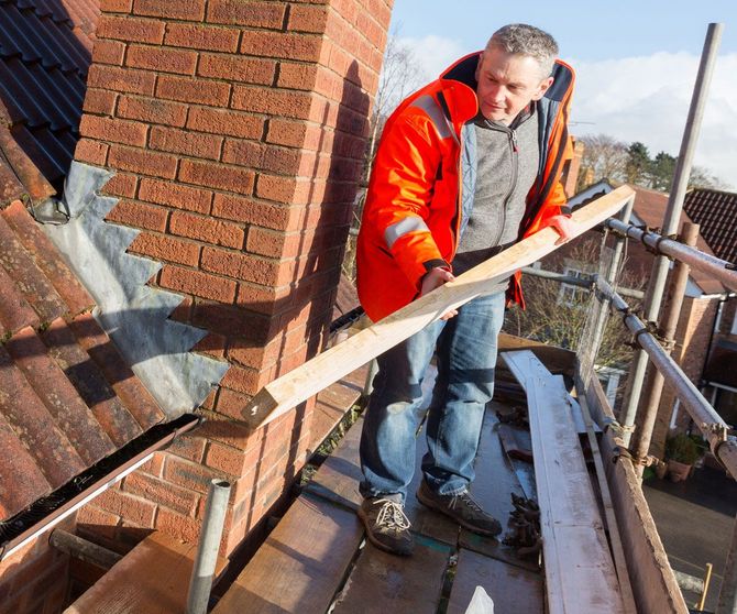 a man in an orange jacket is standing on a scaffolding holding a piece of wood .