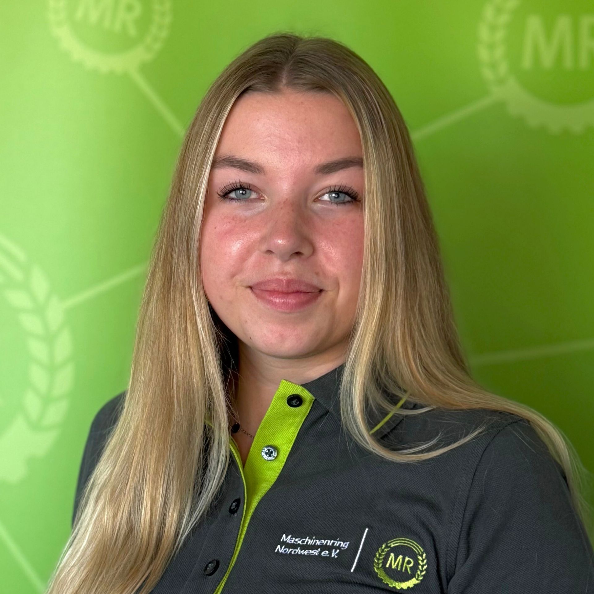 Junge Frau namens Lena Hülts mit blonden langen Haaren, trägt ein graues Hemd mit grünem Kragen und lächelt in die Kamera.