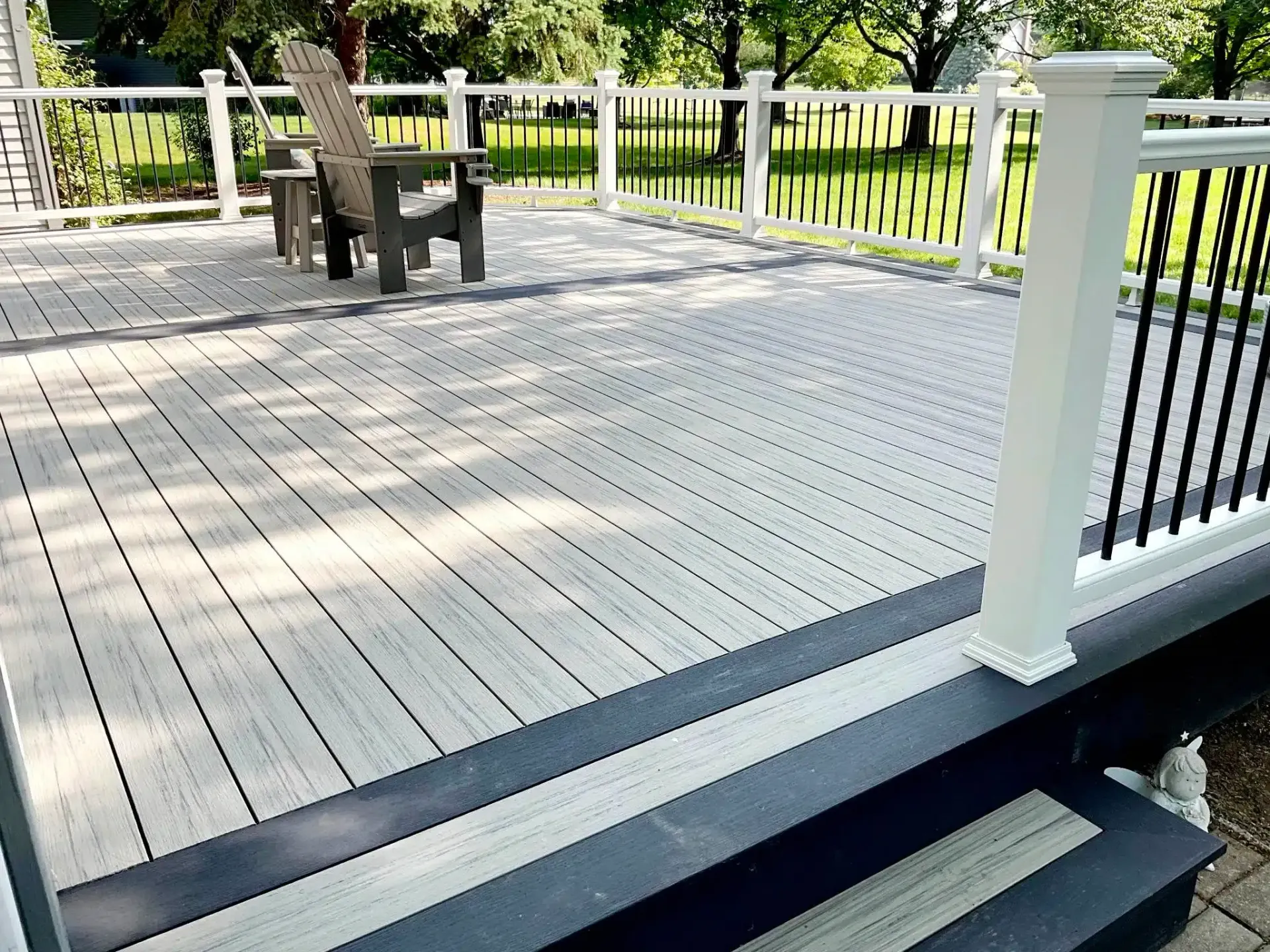 A wooden deck with a white railing and chairs on it.