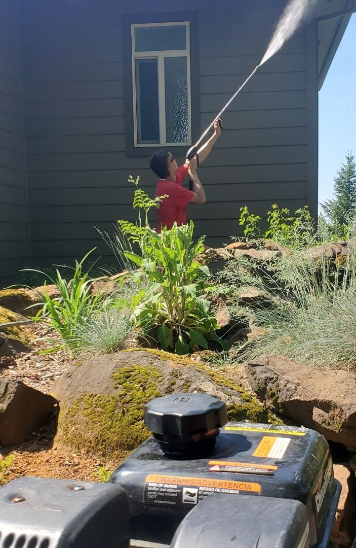 A man is using a pressure washer to clean the side of a house.