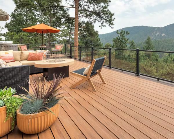 A wooden deck with a couch , chairs , umbrella and potted plants.