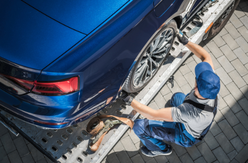 A man is working on a blue car on a tow truck.