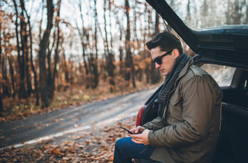 A man is sitting in the back of a car looking at his cell phone.