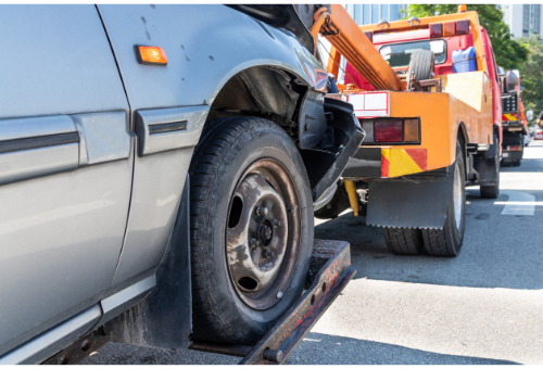 A car is being towed by a tow truck on a city street.