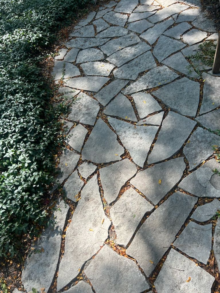 A stone walkway surrounded by bushes and trees in a park.
