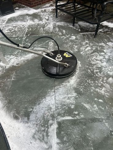 A pressure washer is cleaning a tiled floor on a patio.