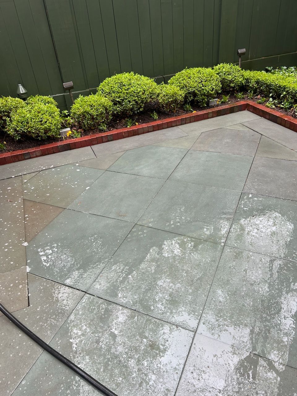 A patio with a fence and bushes in the background.