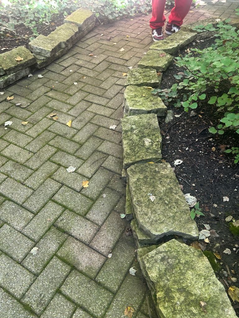 A person is standing on a brick walkway next to a stone wall.