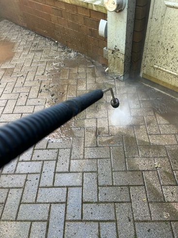 A person is using a high pressure washer to clean a brick walkway.