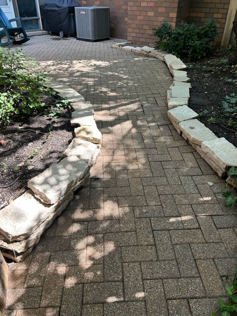 A brick walkway leading to a patio in a backyard.