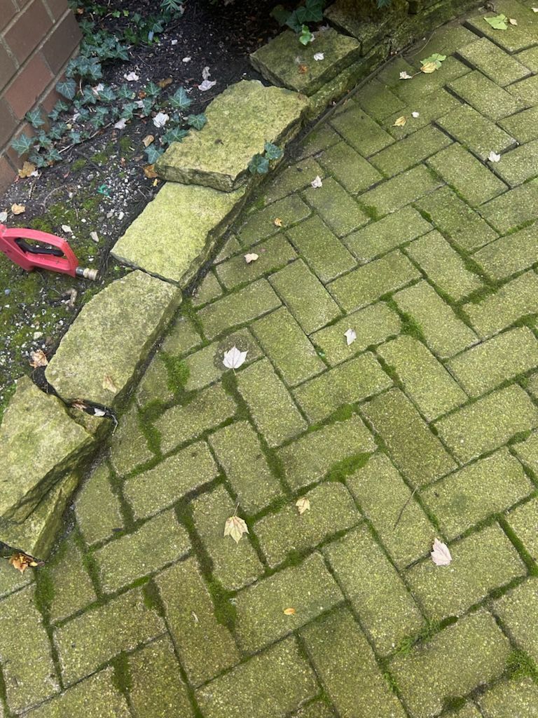 A brick walkway with moss growing on it and a shovel.