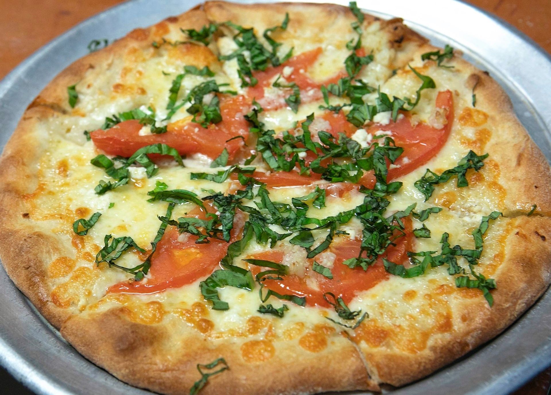 A margherita pizza with cheese, tomatoes and basil on a metal pan