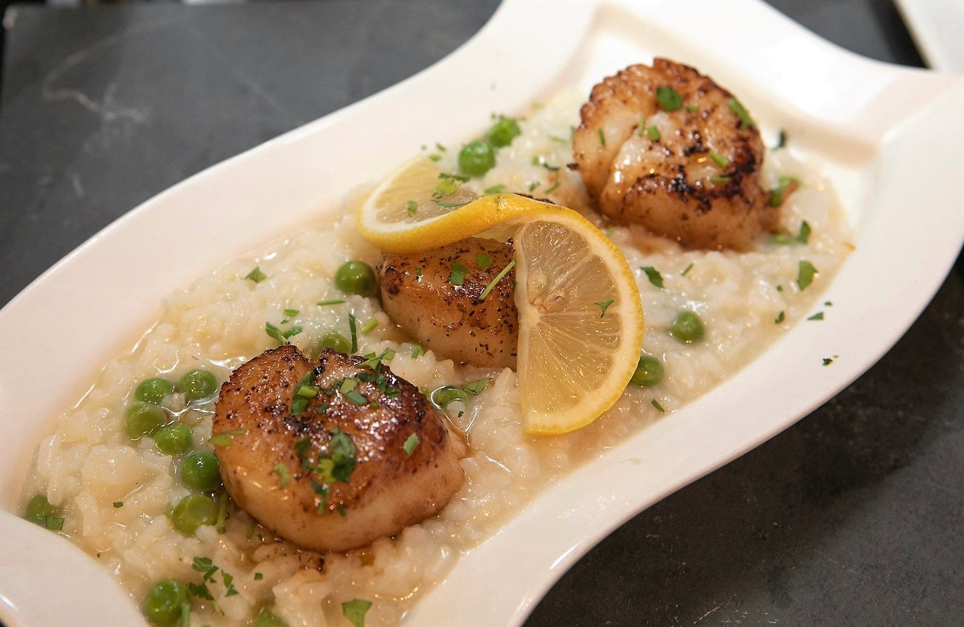 A white plate topped with scallops, risotto and lemon slices.