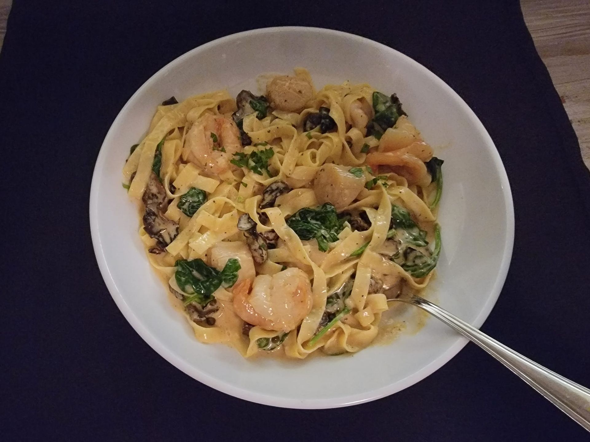 A bowl of pasta with shrimp, scallops and spinach with a fork in it
