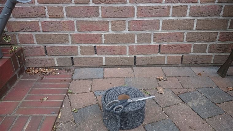 Eine Schere liegt auf einer Rolle Gummiband neben einer Ziegelwand.